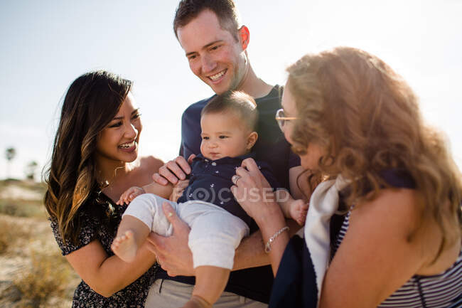 Sonrisas familiares mientras papá sostiene al bebé en la playa - foto de stock