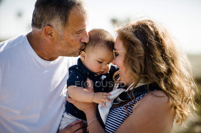Abuelos sonriendo y sosteniendo nieto en la playa - foto de stock