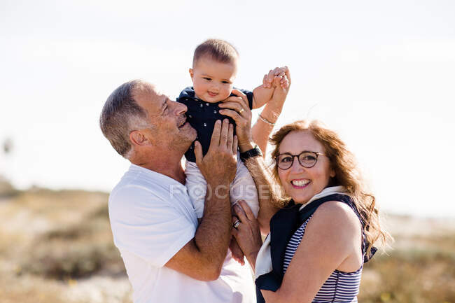 Grand-parents souriant & tenant petit-fils sur la plage — Photo de stock