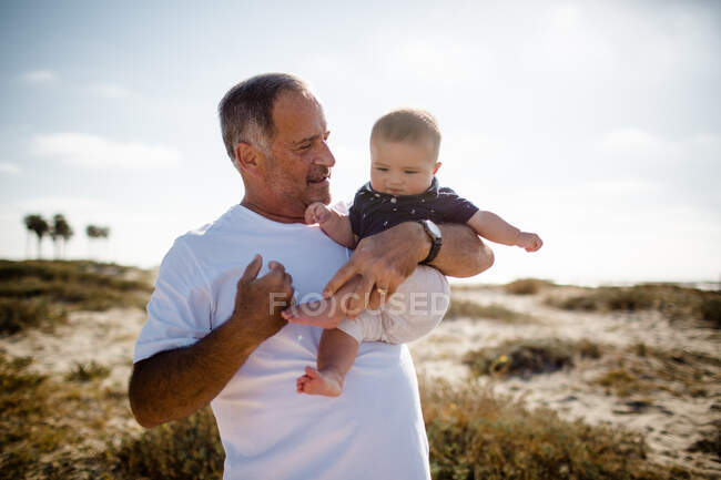 Nonno Holding nipote mentre in piedi sulla spiaggia — Foto stock