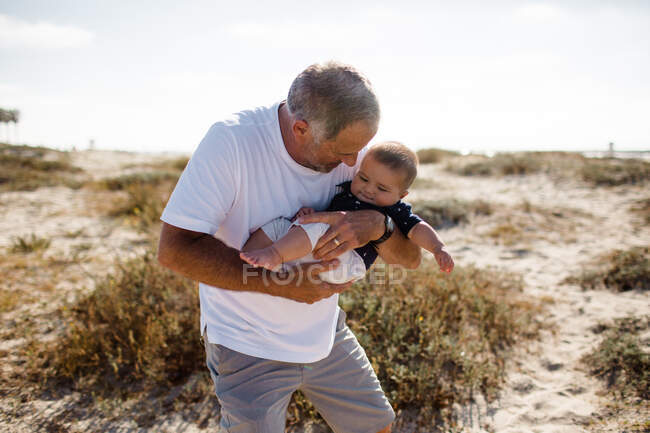 Avô Berço neto enquanto em pé na praia — Fotografia de Stock