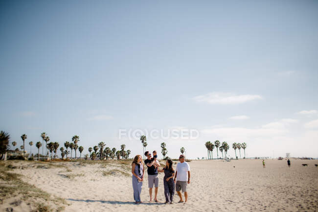Familia de cinco caminando en la playa - foto de stock