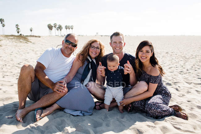 Fünfköpfige Familie sitzt am Strand und lächelt vor der Kamera — Stockfoto