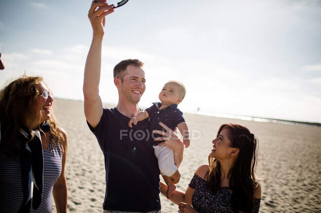 Pai segurando óculos de sol para chamar a atenção do filho enquanto a família sorri — Fotografia de Stock