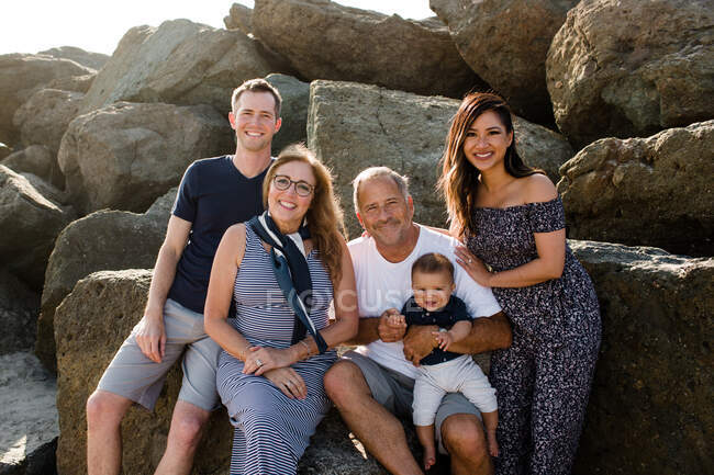 Семья из пяти кузнечиков для камеры, сидящей на скалах на пляже — стоковое фото
