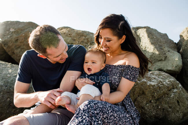 Eltern mit Mitte 30 halten Säugling am Strand auf Felsen — Stockfoto