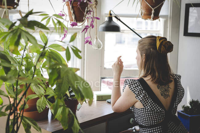 Молодая женщина сидит за столом с растениями и книгами — стоковое фото