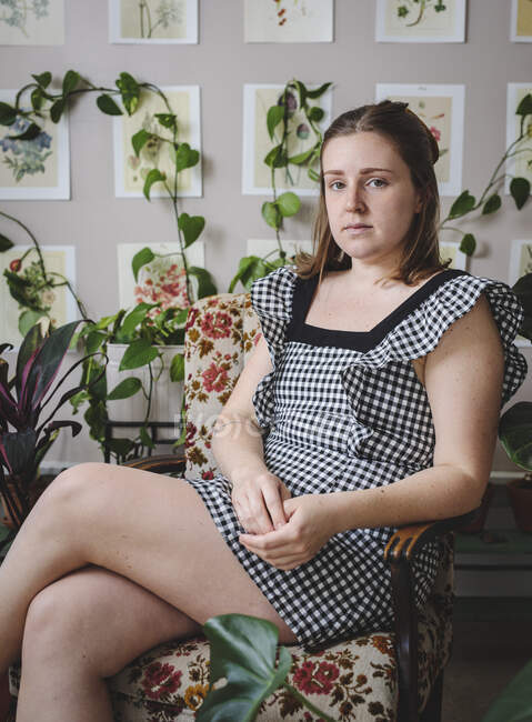 Стильна молода жінка сидить у кріслі перед рослинами та мистецтвом — стокове фото