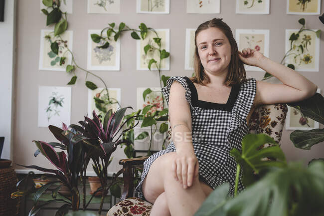 Stylish young woman smiles while sitting in chair with plants — Stock Photo