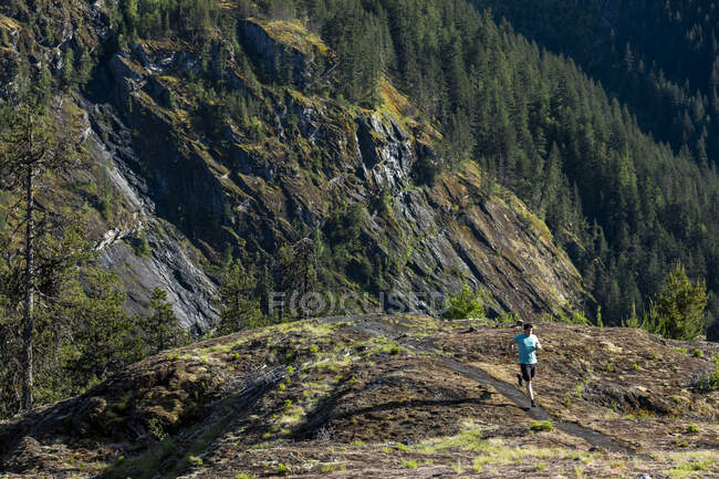 Un sentiero uomo corre su un sentiero di montagna con vista panoramica sulle montagne costiere della Columbia Britannica in una giornata di sole primaverile. — Foto stock