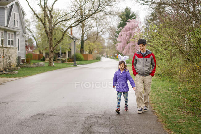Una niña con orejas de conejo camina con su padre en la calle en primavera - foto de stock