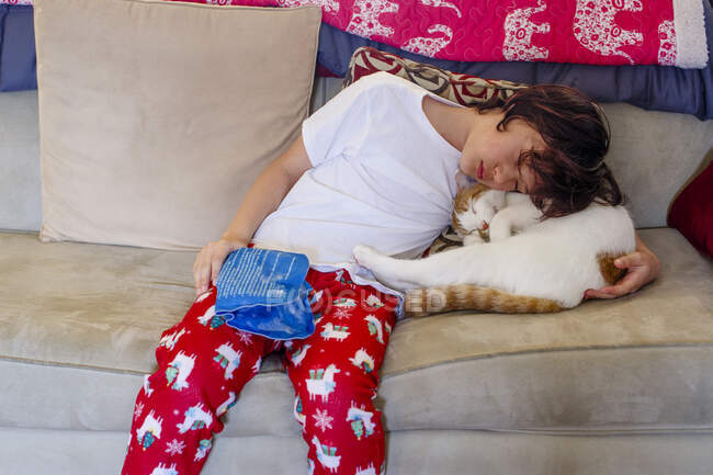 Un niño con la mano lesionada sostiene una bolsa de hielo y se acurruca gato para mayor comodidad - foto de stock