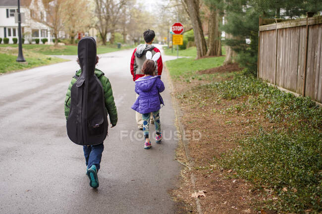 Un chico llevando un violonchelo camina con su familia por la calle suburbana - foto de stock