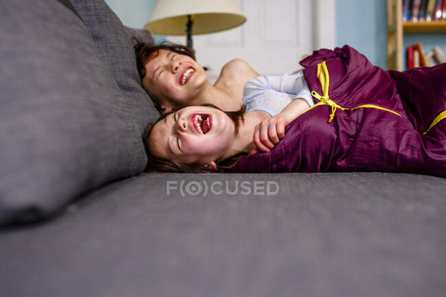 Двоє щасливих дітей лежать на дивані разом сміючись голосно з радістю — стокове фото