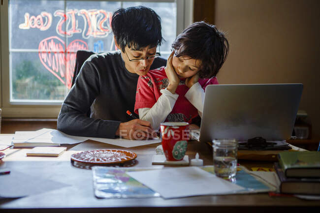 A father works home at the dining room table with his son in his lap — Stock Photo