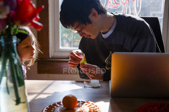 Батько допомагає своїй дитині з паперовим ременем, поки вона уважно спостерігає — стокове фото