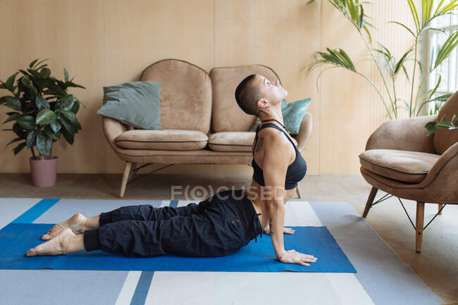 Atlético pele cabeça mulher em cobra ioga bhujangasana pose em casa interior — Fotografia de Stock