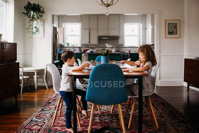 Младшие брат и сестра сидят за обеденным столом, раскрашивая вместе — стоковое фото