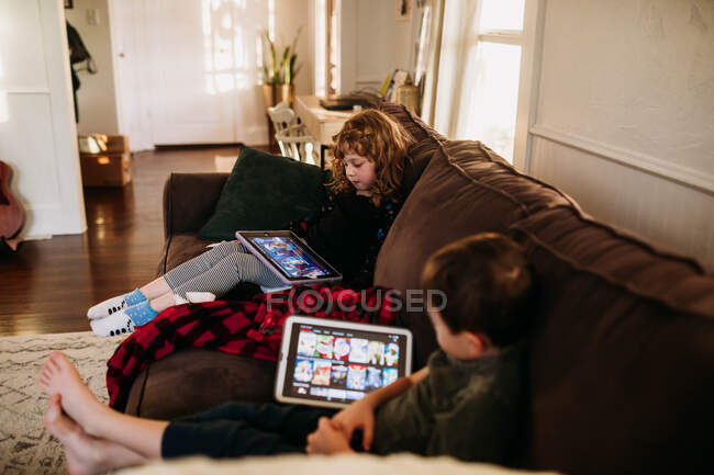 Young sister and brother watching movies on tablets while home sick — Stock Photo