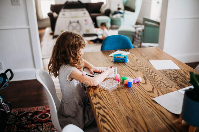 Young girl coloring picture while sitting at dining room table — Stock Photo