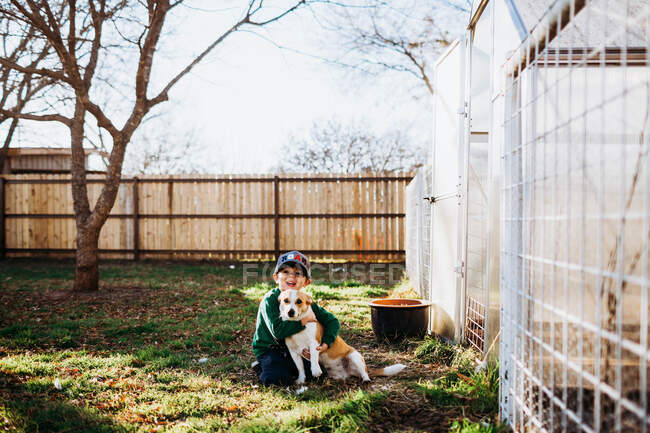 Мальчик улыбается и обнимает собаку на заднем дворе весной — стоковое фото