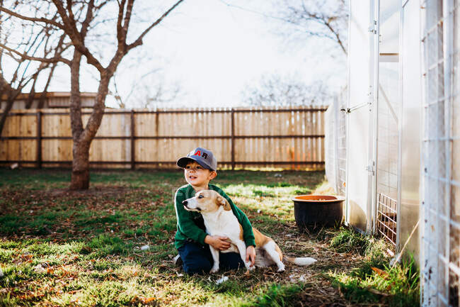 Young boy hugging corgi dog while sitting outside backyard greenhouse — Stock Photo