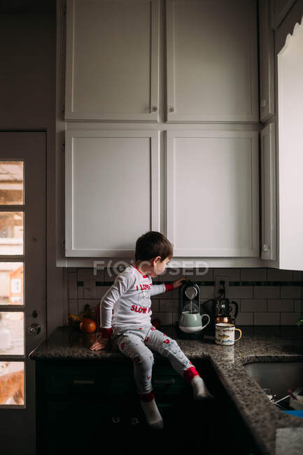 Kleiner Junge sitzt auf einem Tresen und kocht Kaffee — Stockfoto