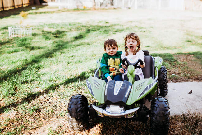 Young boy and girl sitting in powerwheels smiling during spring — Stock Photo