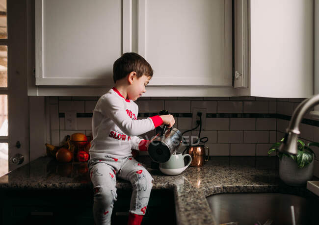 Мальчик наливает пенное молоко в кофейную чашку — стоковое фото