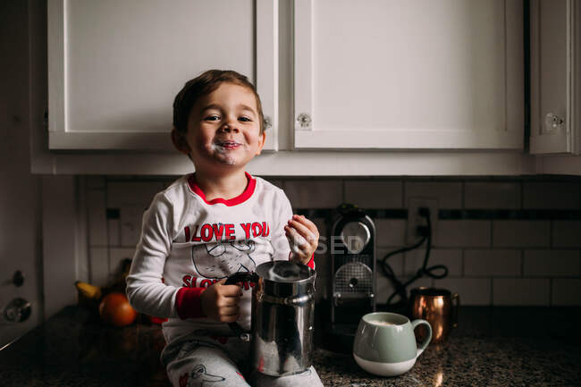 Young boy sitting on kitchen counter with frothed milk on face — Stock Photo