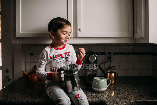 Preschool age boy sitting on a kitchen counter with milk on his face — Stock Photo