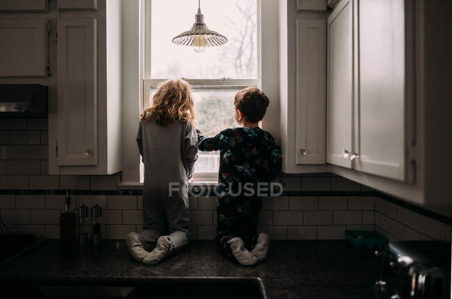 Frère et sœur regardant par la fenêtre de la cuisine — Photo de stock