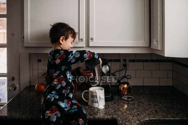 Jovem menino derramando leite na xícara de café — Fotografia de Stock