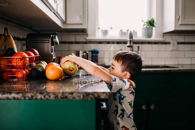Jovem menino chegando para frutas no balcão da cozinha — Fotografia de Stock