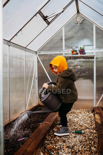 Young boy watering seeds in backyard green house — Stock Photo