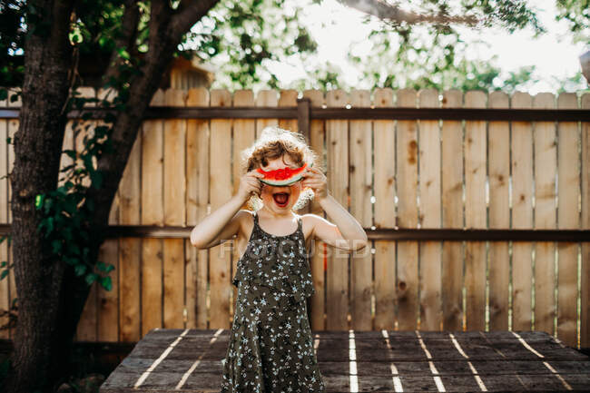 Giovane ragazza sorridente e si nasconde dietro fetta di anguria in primavera — Foto stock