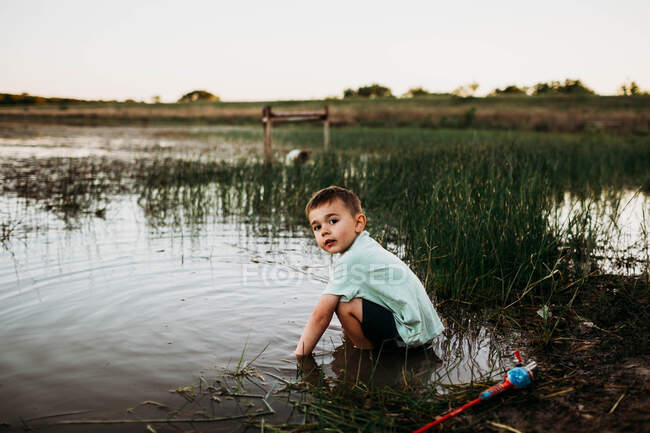 Молодий хлопець сидить в озері, намагаючись ловити рибу — стокове фото