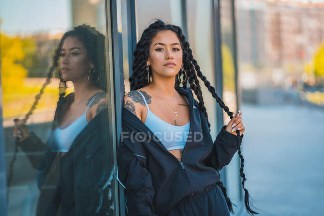 Young black girl leaning against a glass touching the braids — Stock Photo