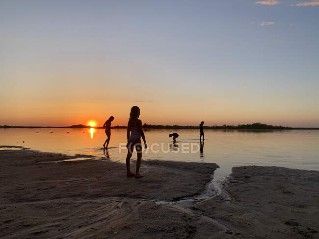 Силует дітей на пляжі на заході сонця — стокове фото