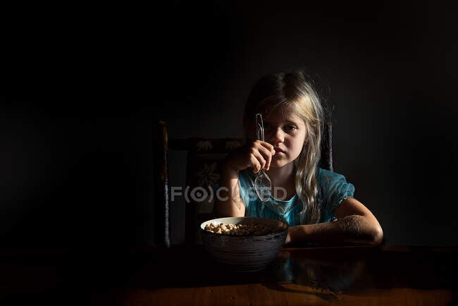 Маленькая девочка ест хлопья в ярком свете, глядя в камеру — стоковое фото