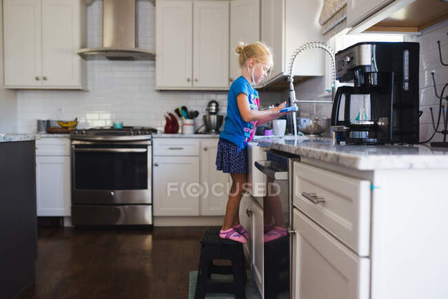 Маленькая девочка у раковины моет посуду — стоковое фото