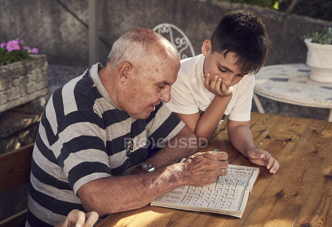 Хлопець з дідусем роблять кросворди. — стокове фото