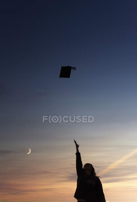 Silueta de estudiante universitario lanzando gorra de graduación al aire - foto de stock