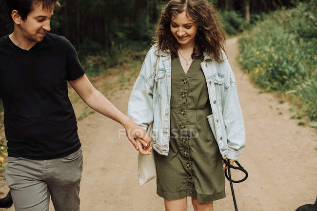 Pareja joven en la primera cita cogida de la mano mientras camina por el camino - foto de stock