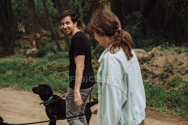 Young man looking back over shoulder at a woman while walking dogs — Stock Photo
