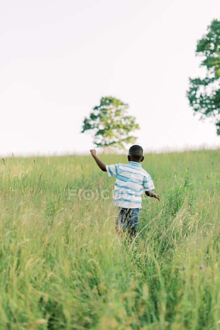 Солодкий маленький хлопчик біжить через луг на заході сонця — стокове фото