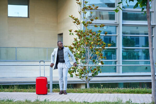 Afro-Américain en costume blanc et une valise rouge. Homme d'affaires. Homme d'affaires voyageant pour affaires. Un voyageur. — Photo de stock