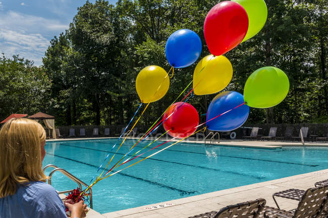 Visão traseira de uma jovem segurando um conjunto de balões coloridos — Fotografia de Stock