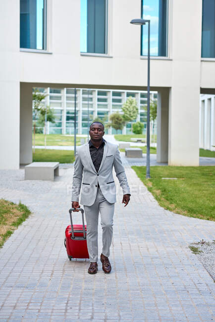 Afroamerikaner in weißem Anzug und rotem Koffer. Geschäftsmann. Geschäftsmann auf Geschäftsreise. Reisender Mann. — Stockfoto