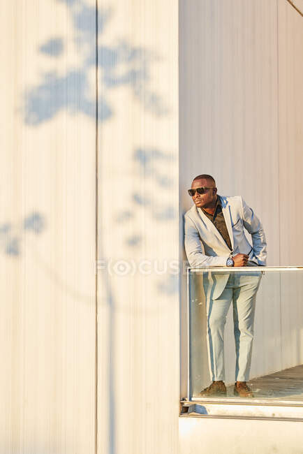 Афроамериканский бизнесмен на закате в здании. Он купается под вечерним солнцем. Тень дерева проецируется на стену — стоковое фото